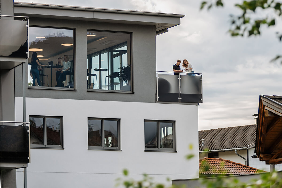 Mitarbeiter stehen auf dem Balkon des Firmengebäudes und unterhalten sich