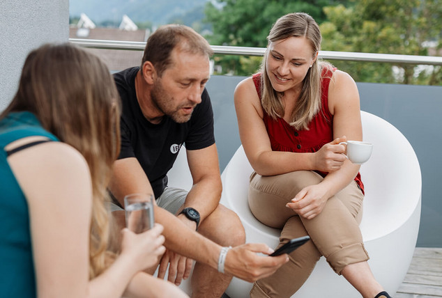 Eine Gruppe von Mitarbeitern sitzen lächelnd und schauen in ein Mobiltelefon