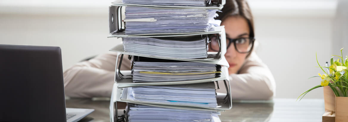 Mitarbeiterin blickt hinter einem Stapel Ordner hervor