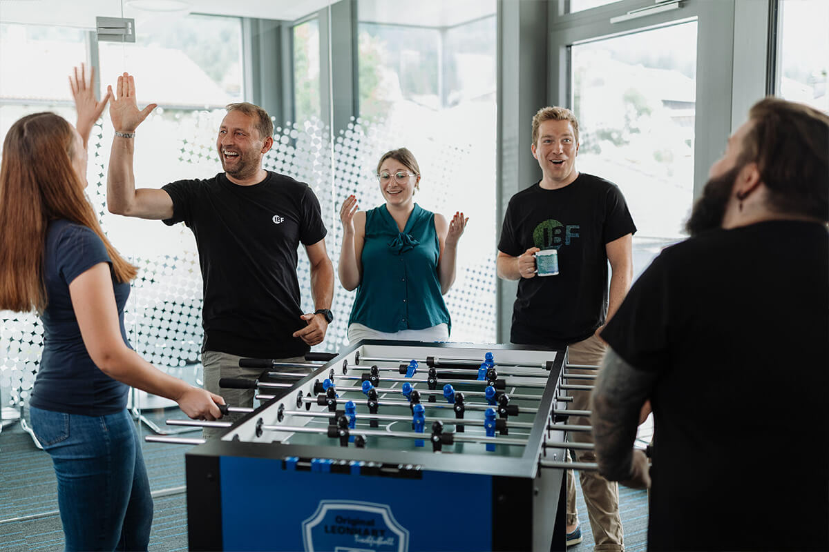 Gruppe von Mitarbeitern stehen jubeln an einem Tischfußballtisch